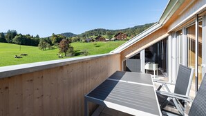 A balcony with a table and chairs, overlooking a green field and houses in the distance. - Rose house in Schwarzenberg (Schwarzenberg)