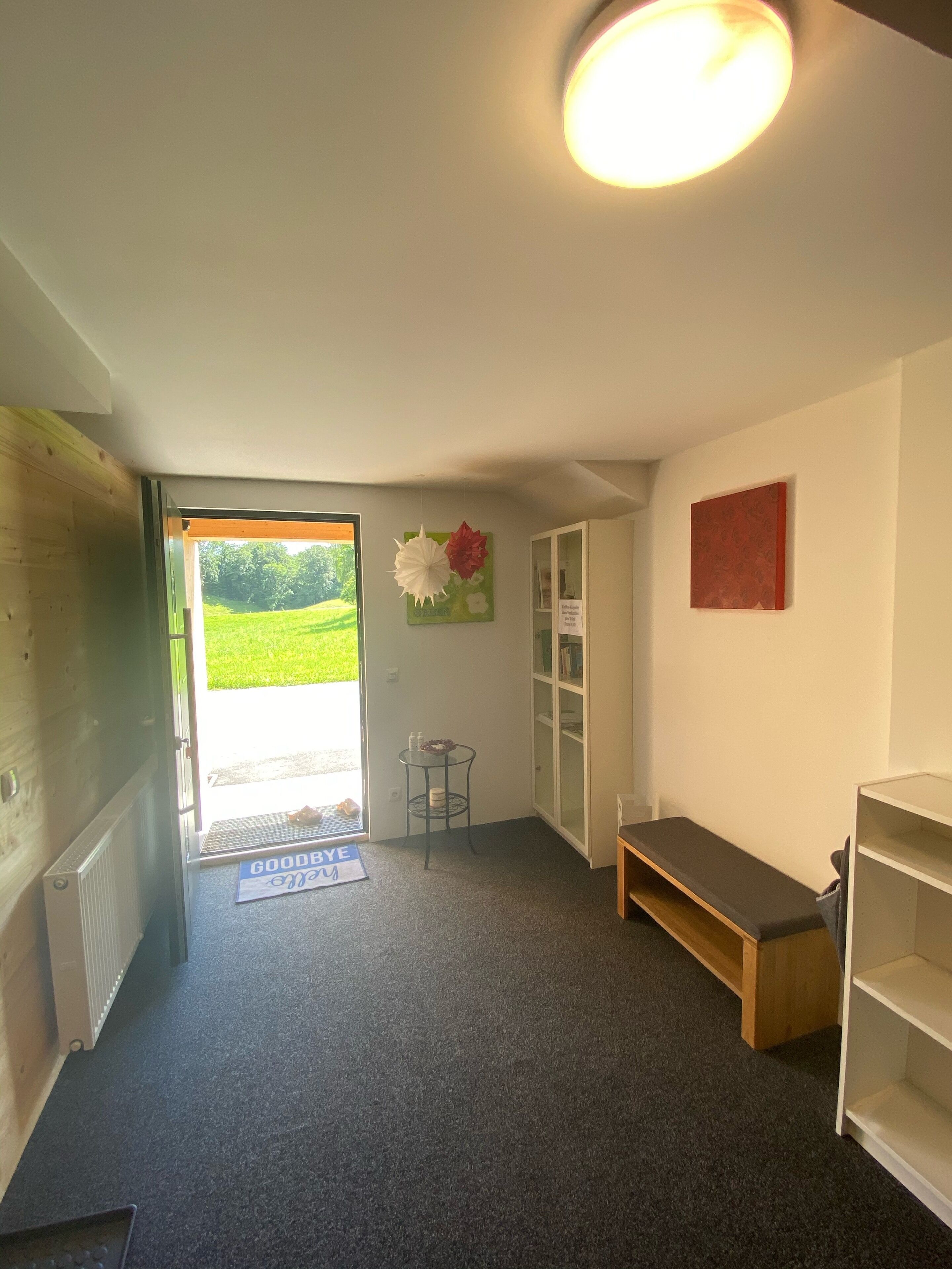 Una habitación con un banco, una mesa pequeña, un radiador y una puerta que da al exterior.