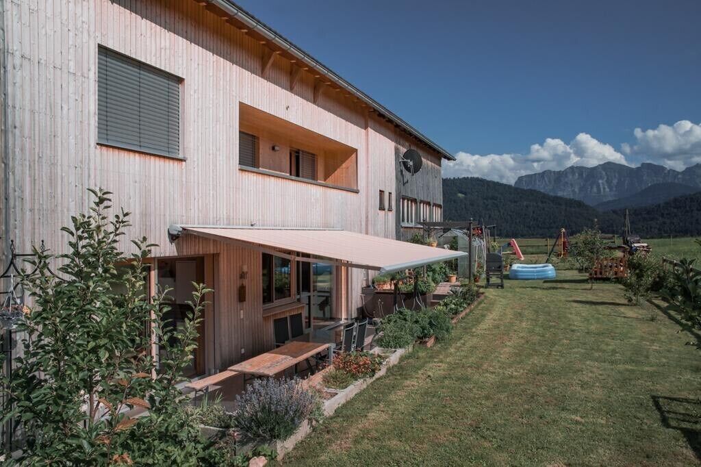 Una casa moderna de dos pisos con un patio, un comedor y vistas a las montañas.