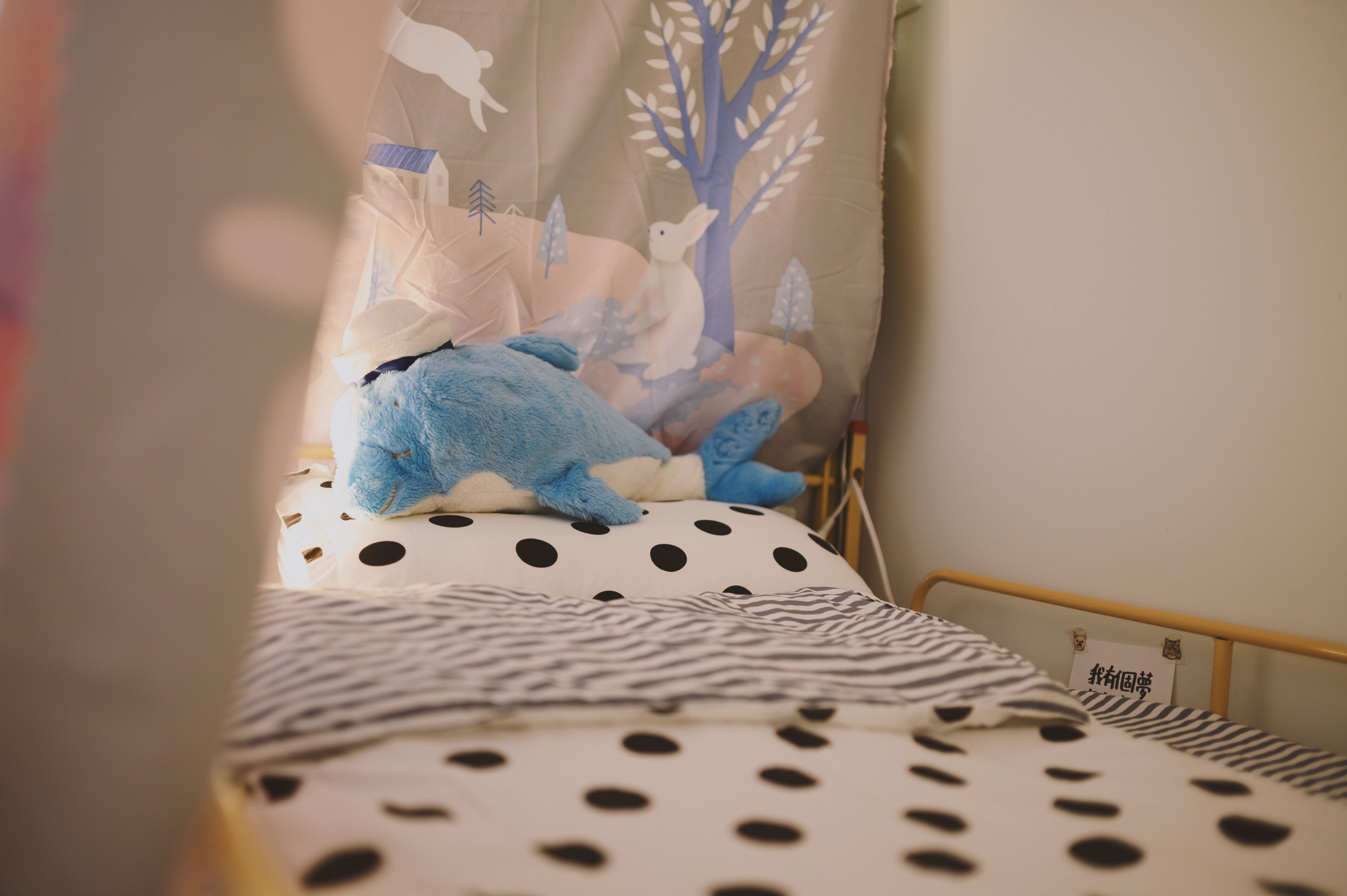 Una cama con un edredón de lunares y rayas, una almohada con un diseño de árboles y animales, y un letrero pequeño con caracteres japoneses.