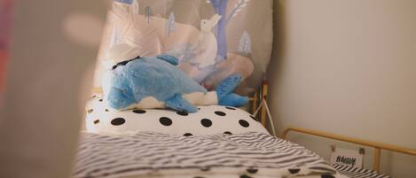 Una cama con un edredón de lunares y rayas, una almohada con un diseño de árboles y animales, y un letrero pequeño con caracteres japoneses.