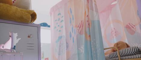 A child's bunk bed with a striped blanket and a stuffed animal, a whiteboard with drawings and a cat sticker, and a pink curtain with abstract patterns.