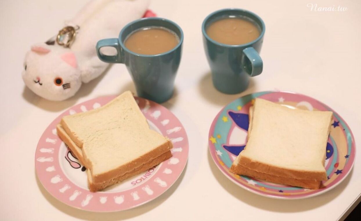 Two plates of white bread on a table with two blue cups of coffee and a white cat-shaped keychain.