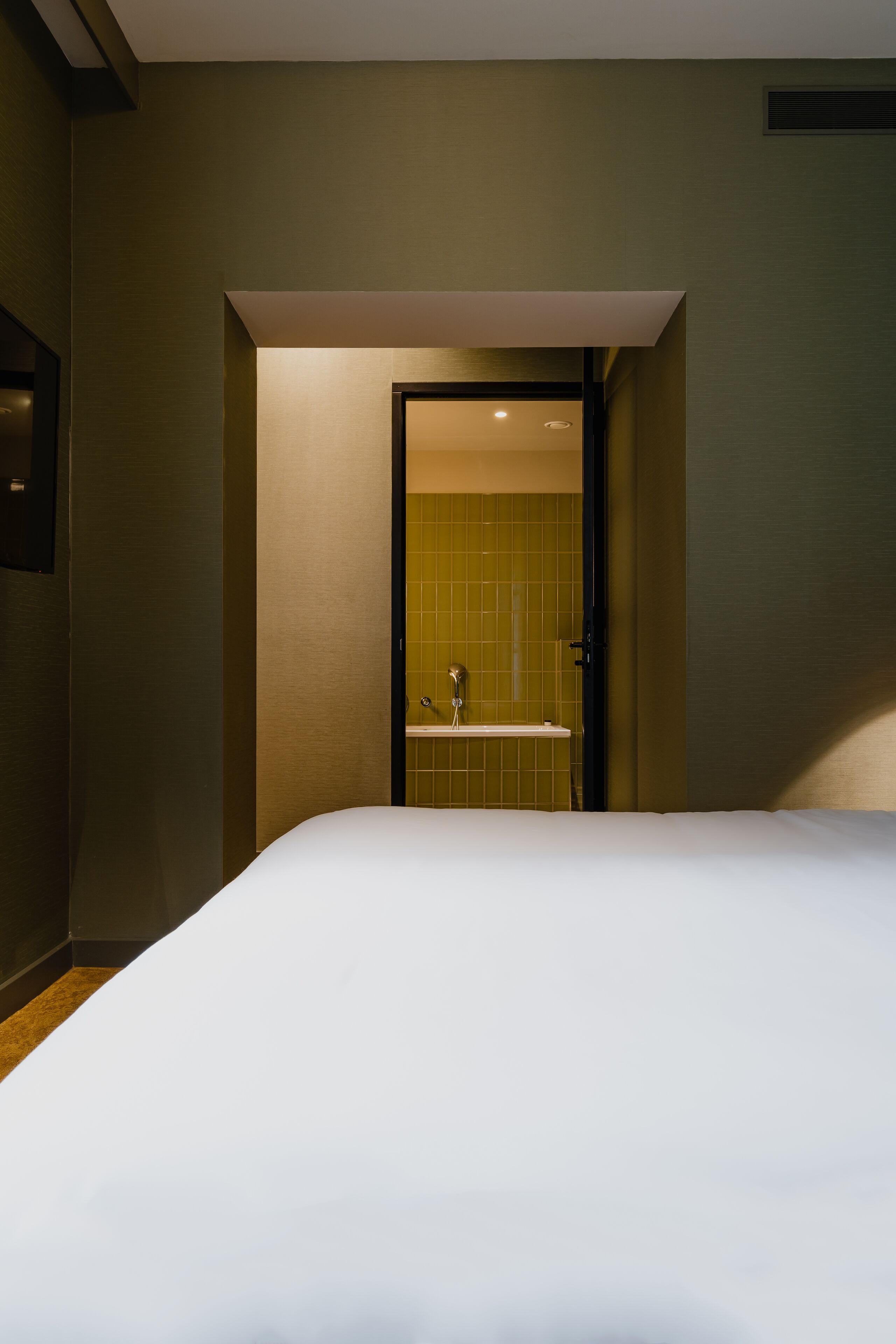 A hotel room with a large bed, a bathroom with a shower, and a door leading to another room.
