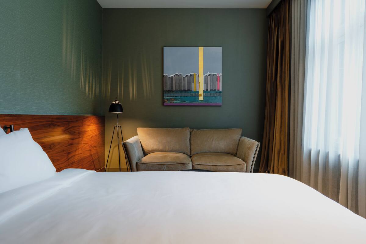 Ein Hotelzimmer mit Bett, Sofa, Lampe und einem Gemälde an der Wand.