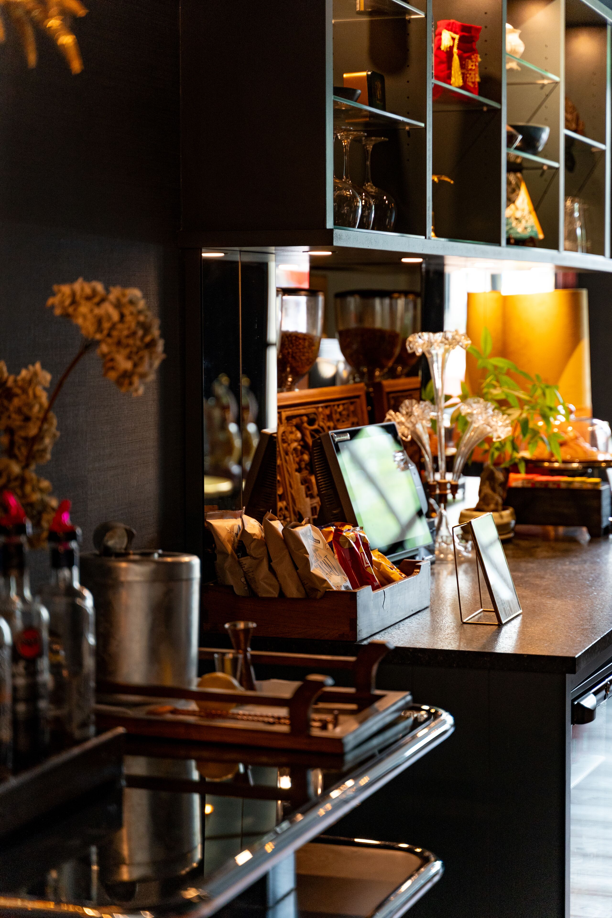 A bar area with a counter, shelves, and various items including a cash register, bottles, and decorative objects.