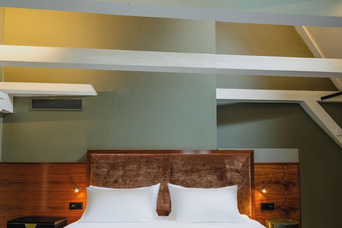 Ein Hotelzimmer mit einem großen Bett, einem Holzkopfstück und Blick zum Himmel durch ein offenes Fenster.