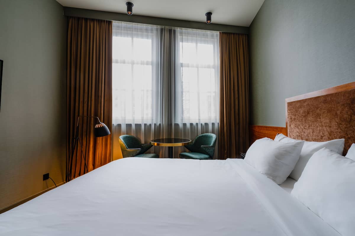 Ein Hotelzimmer mit einem großen Bett, zwei Sesseln, einem kleinen Tisch und einem Fenster mit Vorhängen.