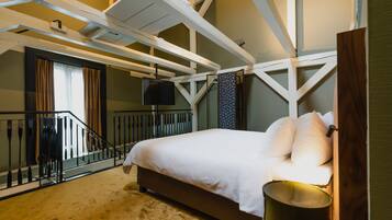 Un dormitorio con una cama, cabecera de madera, ventana con cortinas, una escalera y un televisor montado en la pared.