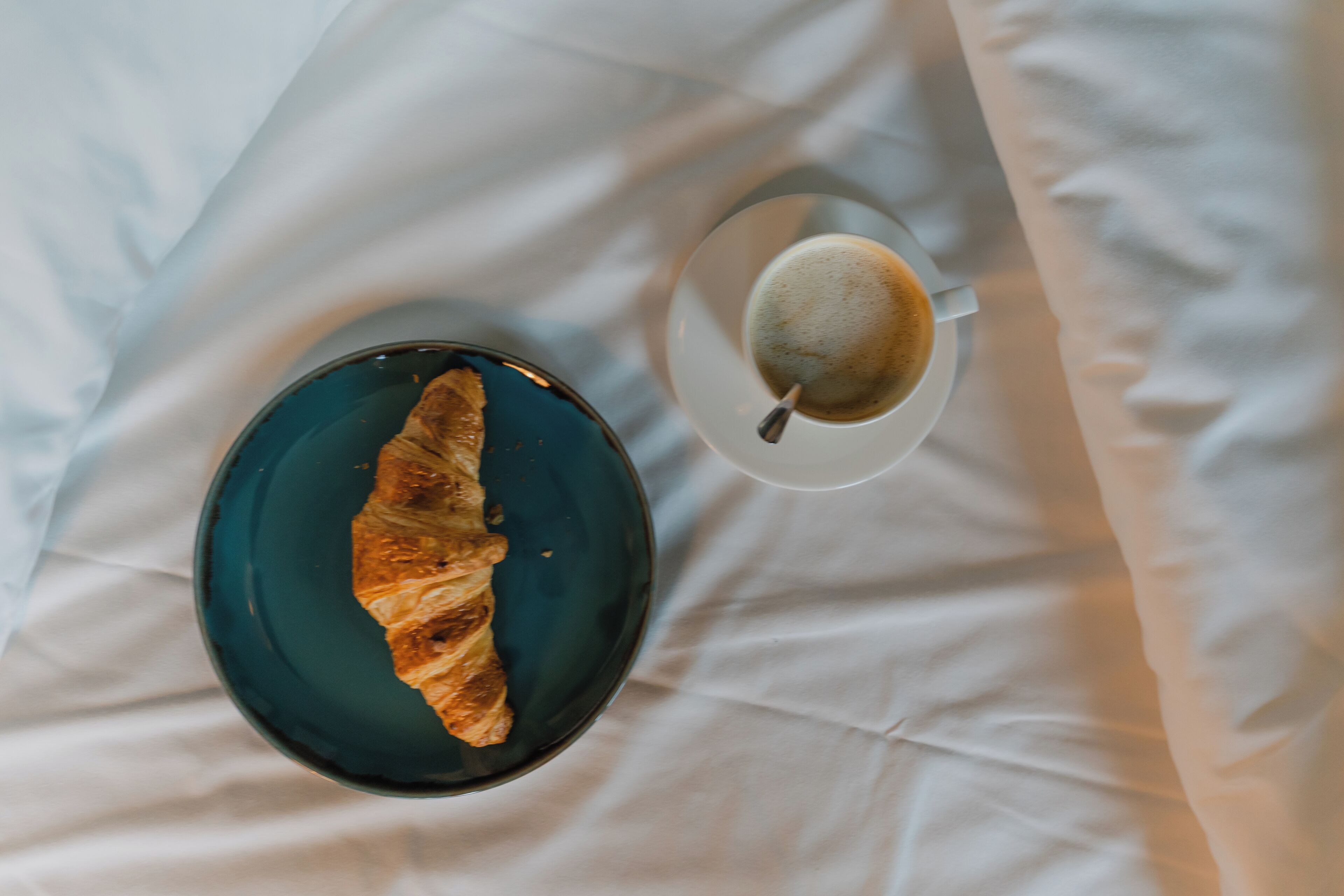 Un croissant sur une assiette bleue et une tasse de café sur une nappe blanche.