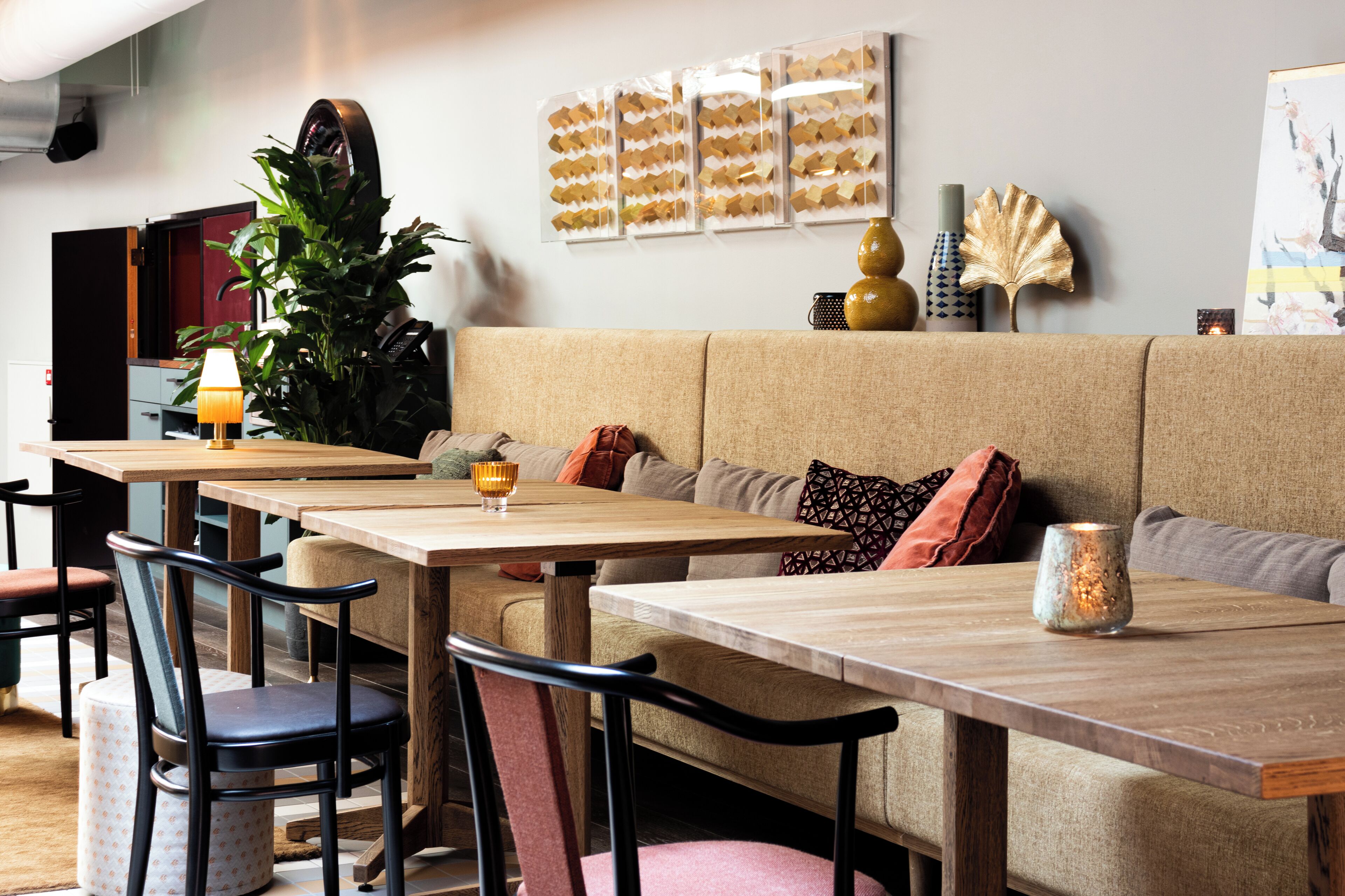 Un espace repas moderne avec des tables et des chaises en bois, un canapé avec des coussins et un mur agrémenté d’objets décoratifs.