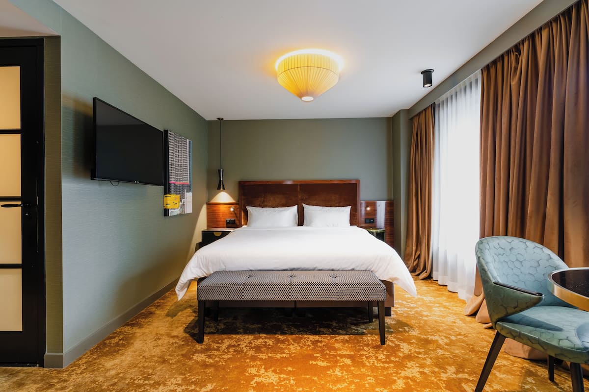 Ein Hotelzimmer mit einem großen Bett, einer Bank, einem Sessel, einem Fernseher und einer Deckenleuchte.