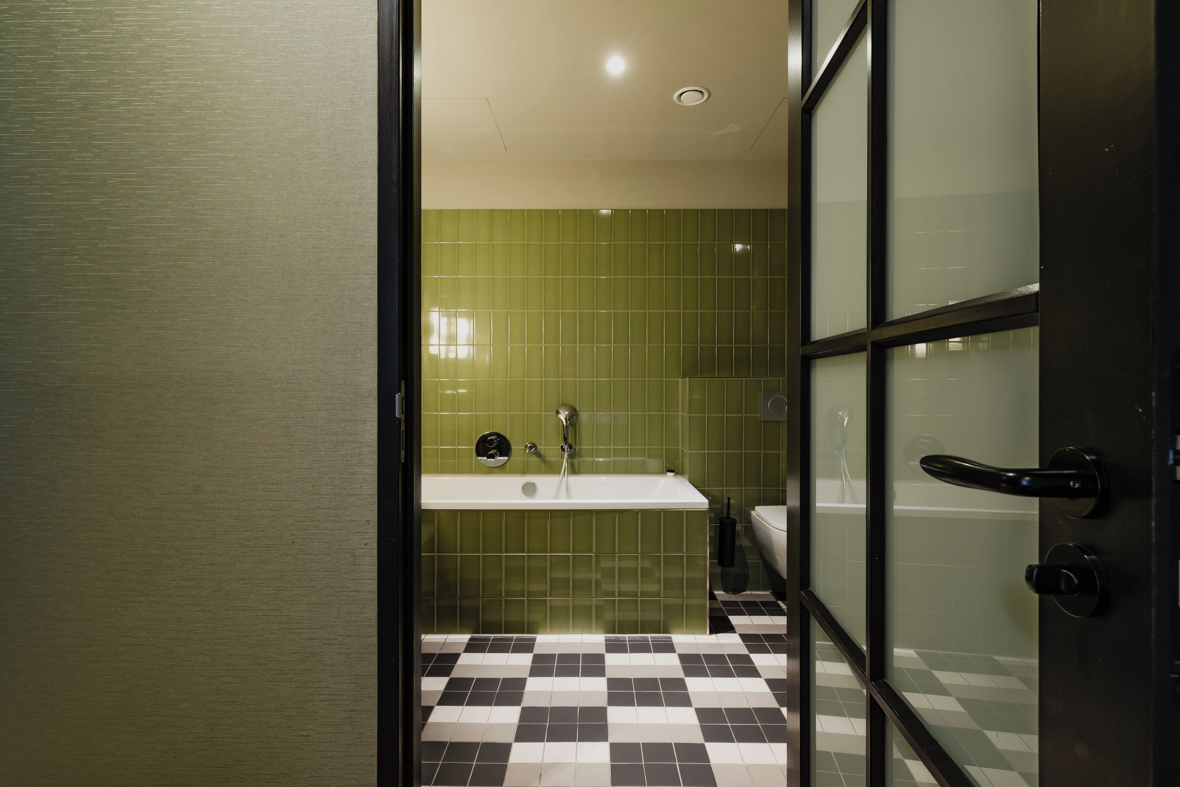 Un baño con suelo a cuadros, un lavamanos blanco y azulejos verdes en las paredes.