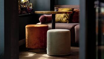 A cozy seating area with a cushioned bench, a round ottoman, and a small table with a lamp.