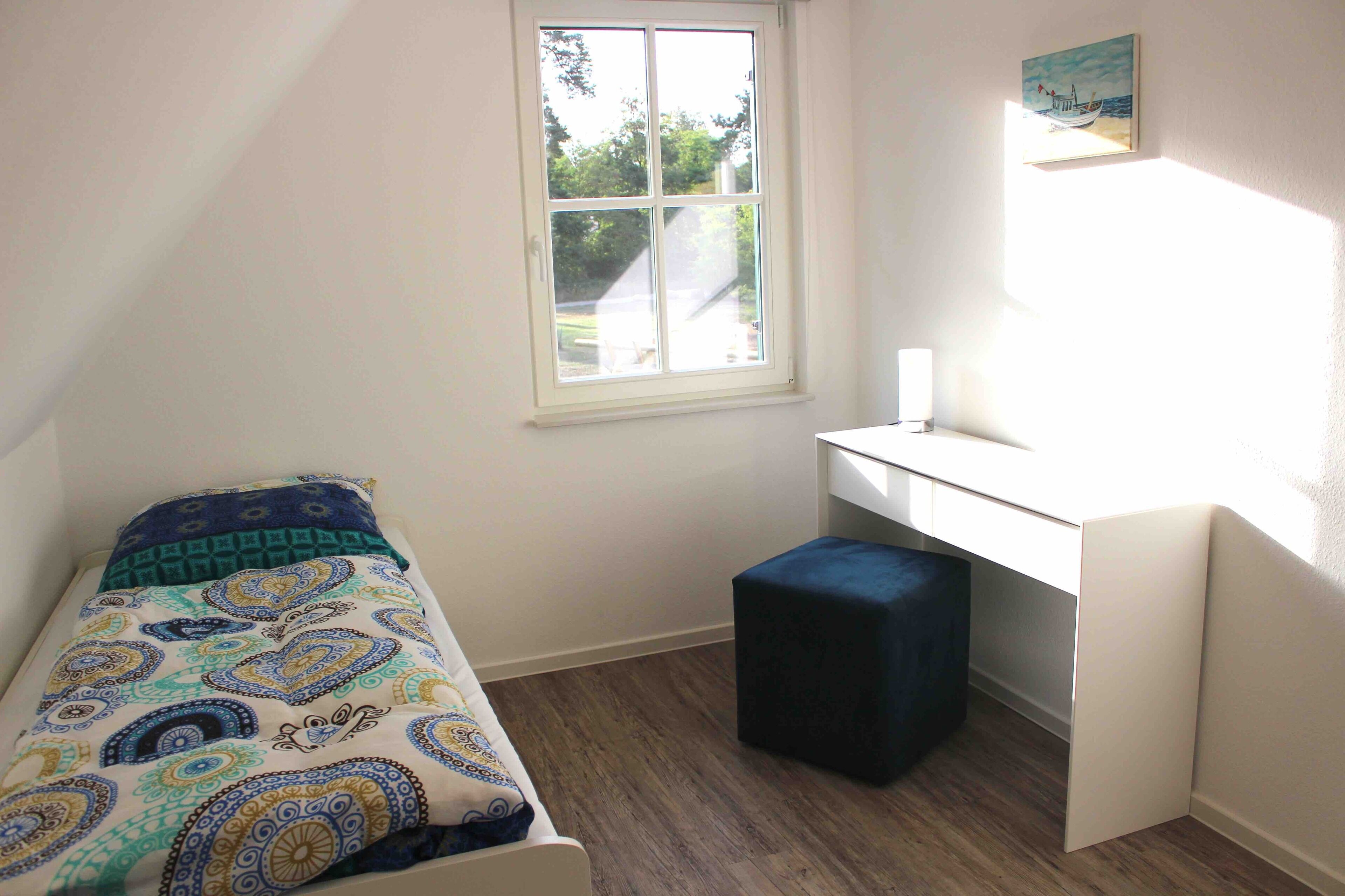 Een kleine, verzorgde slaapkamer met een enkel bed, een bureau en een raam dat voor natuurlijk licht zorgt.