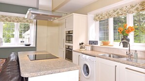 A modern kitchen with built-in appliances, a granite countertop, and a window with a view of greenery. - Little Friston Lodge (Eastbourne)