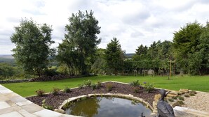 A landscaped garden with a pond, stone pathway, and a view of the surrounding landscape. - Little Friston Lodge (Eastbourne)