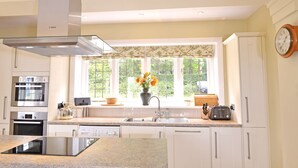A modern kitchen with white cabinetry, a Bosch oven, a dishwasher, a built-in stove, a large window with a view of greenery, and a clock on the wall. - Little Friston Lodge (Eastbourne)