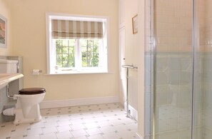 Ein Badezimmer mit Toilette, einem Fenster mit gestreifter Vorhangschlaufe und einer Dusche mit Glastür sowie gefliestem Boden mit Muster.