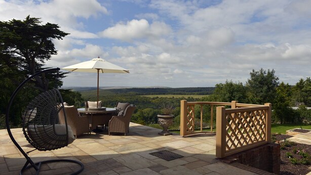 An outdoor patio with a wicker table and chairs, a hanging chair, and a wooden fence. - Little Friston Lodge (Eastbourne)