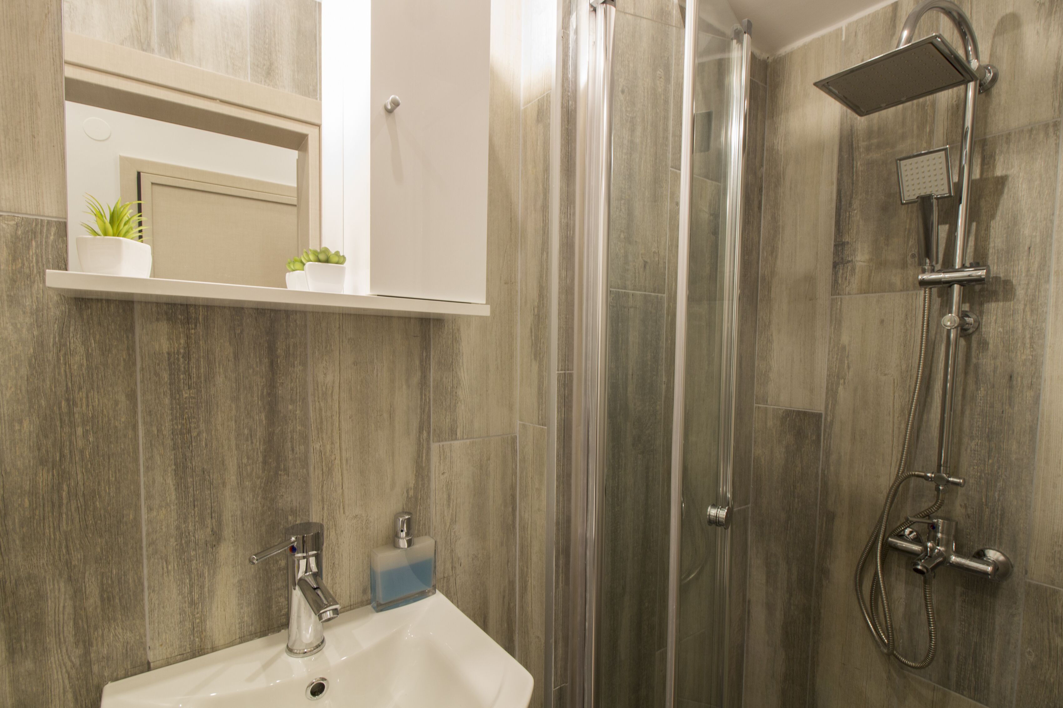 A bathroom with a glass-enclosed shower, a white sink, and a mirror above the sink.
