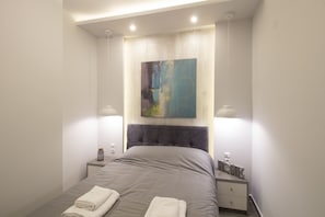 A modern bedroom with a large bed, two bedside tables, a wall-mounted painting, and a ceiling light fixture.
