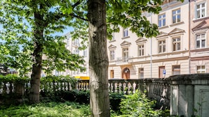 Une cour bordée d’arbres, avec un mur de pierre et, au fond, un bâtiment à l’architecture classique.