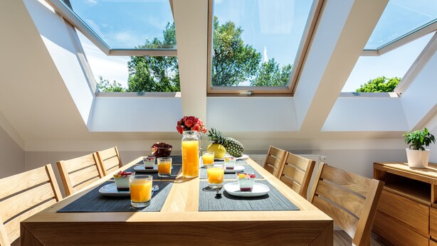Un espace repas avec une table haute, des chaises et une vue sur la verdure grâce à des fenêtres de toit.