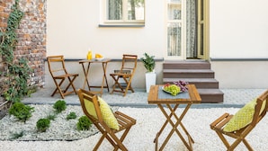 Un espace extérieur aménagé avec des chaises et une table en bois, un petit jardin avec des galets blancs et un mur de briques recouvert de lierre.
