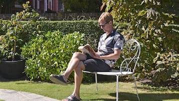 Um homem sentado num banco de metal num jardim, lendo um livro.