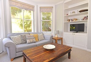 A living room with a grey sofa, a wooden coffee table, and a TV on a white cabinet. - Littledale Haven (Eastbourne)