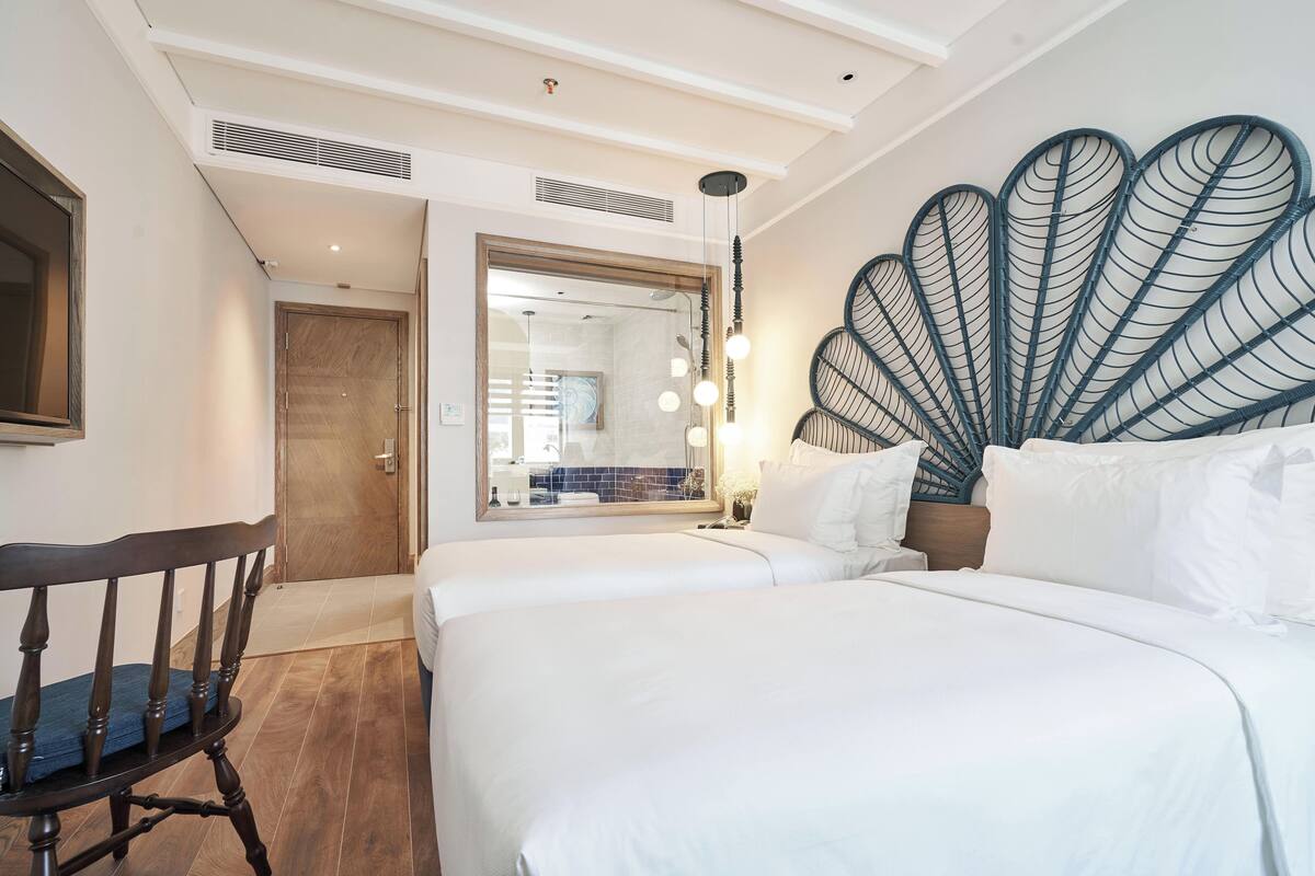 Ein Hotelzimmer mit zwei Betten, einem Holzstuhl, einem Spiegel und einer Wanddekoration.