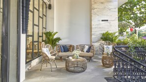Un espace extérieur aménagé avec des meubles en osier, une table basse ronde et un escalier doté d’une rampe en fer forgé.