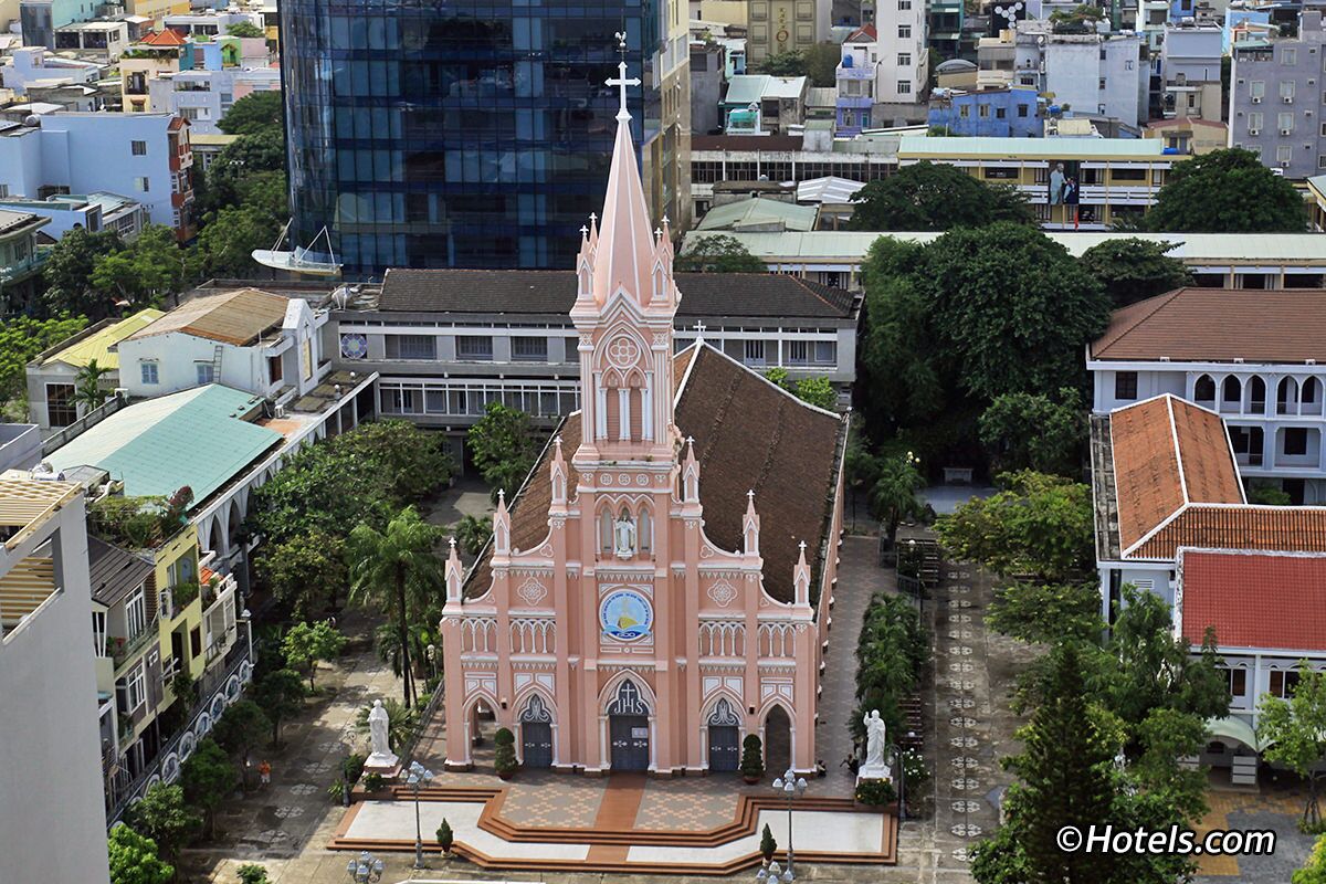 Una iglesia rosada con una torre de reloj, rodeada de árboles y edificios.
