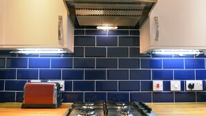 A kitchen with a gas stove, a red toaster, and blue-tiled backsplash. - The Lock (Eastbourne)