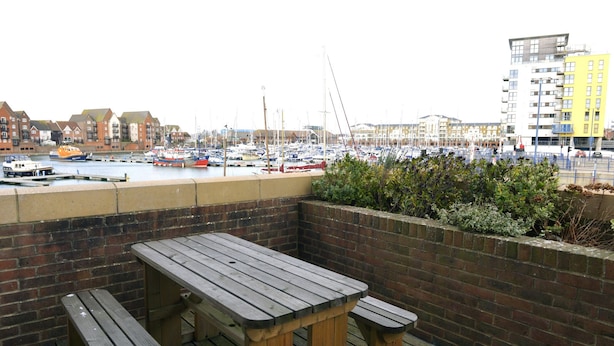 A wooden deck with a bench overlooking a marina with boats. - The Lock (Eastbourne)
