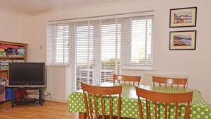 A dining area with a table covered in a green polka dot tablecloth, wooden chairs, a television on a stand, and a bookshelf with various items. - The Lock (Eastbourne)