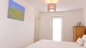 A bedroom with a bed, a wooden wardrobe, a painting, and a ceiling light. - The Lock (Eastbourne)