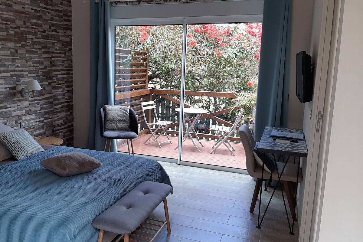 Un dormitorio con cama, un banco, un escritorio y vistas a un patio exterior con mesa y sillas.