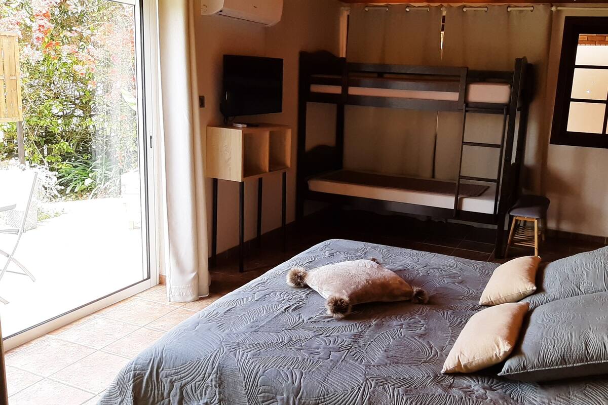 Una habitación con literas, televisión y vistas a un jardín por la ventana.
