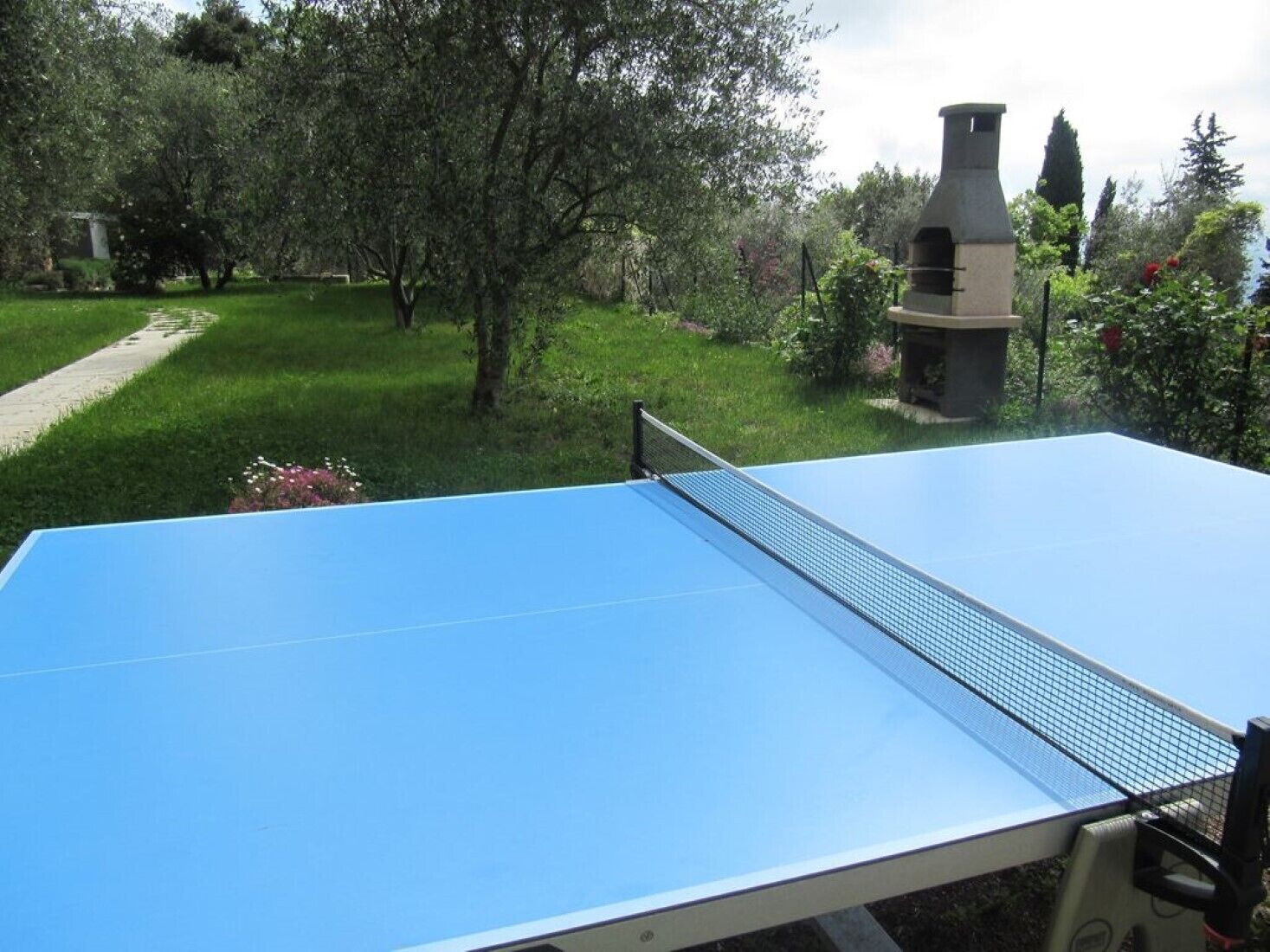 Een tafeltennistafel in een tuin, met een stenen constructie op de achtergrond.