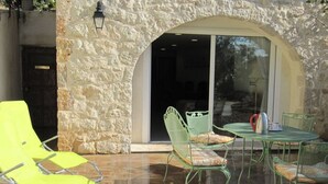 A patio with a stone wall, a glass door, and outdoor furniture including a table, chairs, and a yellow lounge chair. - Cabris, charming Provencal villa, sea view, near the village (Cabris)