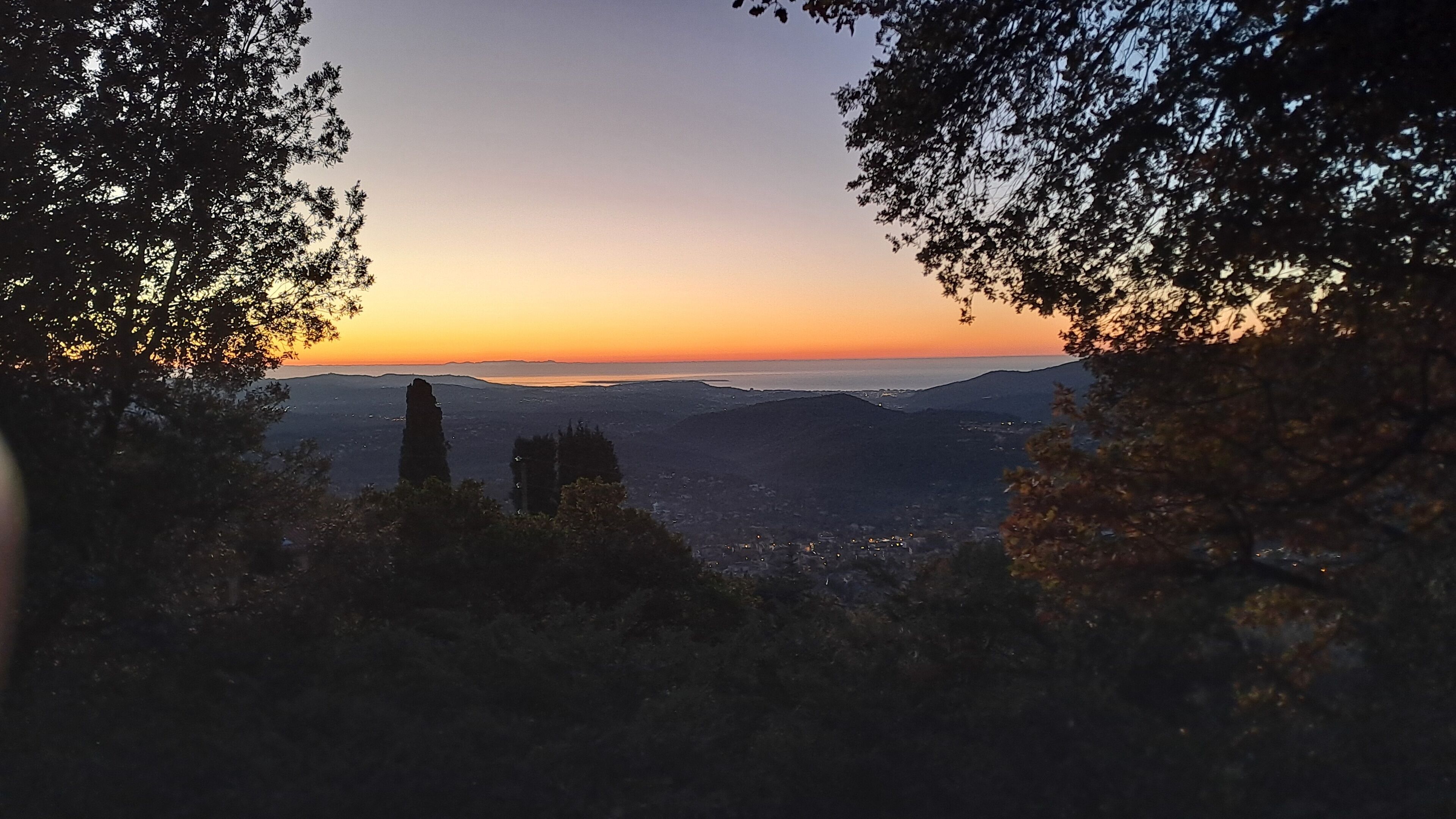 A panoramic view of a city at sunset with a prominent rock formation in the foreground.