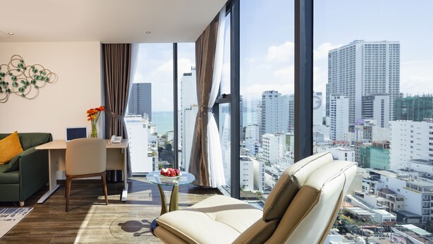 A modern living room with a city view, a sofa, a chair, a small table with a vase, and a desk with a laptop. - Amber Hotel (Nha Trang)