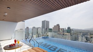 A rooftop infinity pool with a city view, a lounge area with a table, and a glass railing. - Amber Hotel (Nha Trang)