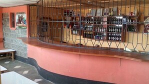 A bar area with a counter, shelves of bottles, and a poster on the wall. - GMT Guest House (Mai Mahiu)