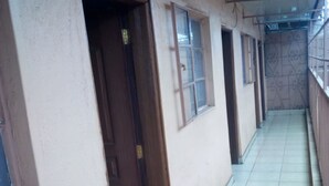 A corridor with tiled flooring, wooden doors, and windows with metal frames. - GMT Guest House (Mai Mahiu)