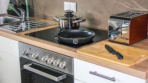 A kitchen with a stove, sink, toaster, and a cutting board with a knife. - EXCLUSIVE 2 room apartment with balcony in top location! (Neustadt)