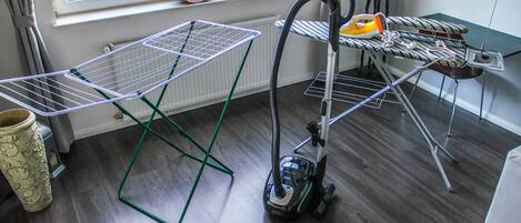 A room with a vacuum cleaner, ironing board, and drying rack.
