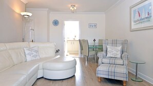 A spacious living room with a white leather sofa, a plaid armchair, and a glass dining table. - Pacific Heights (Eastbourne)